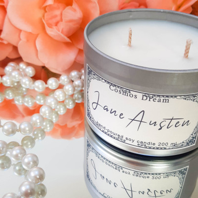 White Jane Austen candle photographed on mirror with pearls and peach colored flowers in the background